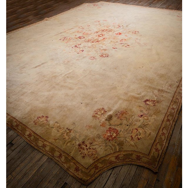 This circa-1925, 13' 2" x 17' 6" European Savonnerie rug eatures a dense, hand-knotted wool pile and a sophisticated beige...