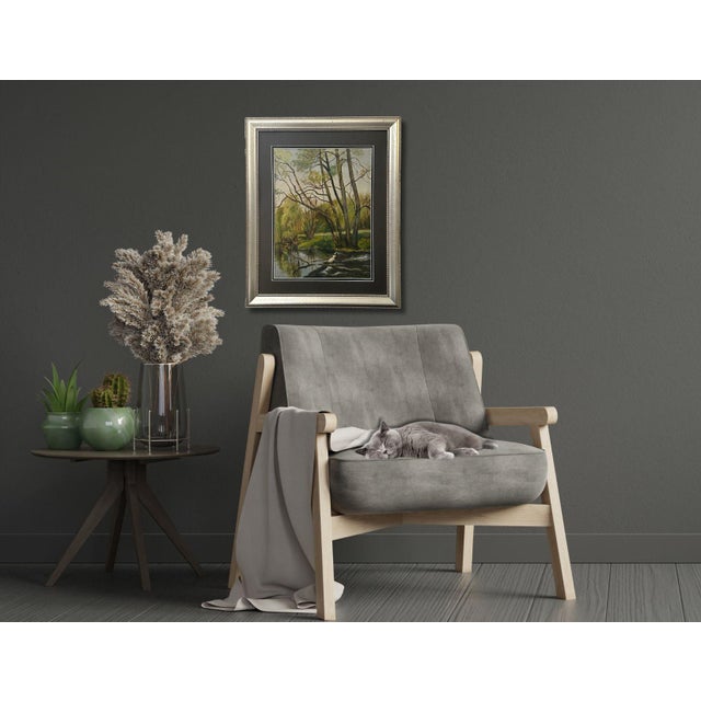 A tranquil French oil on board depicting a serene riverbank where tall trees rise gracefully and lean over the reflective...