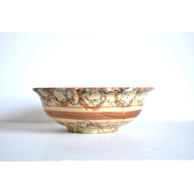 An antique, mid-19th-century large, heavy spongeware mixing bowl in a tan base with brown stripes and brown and blue...