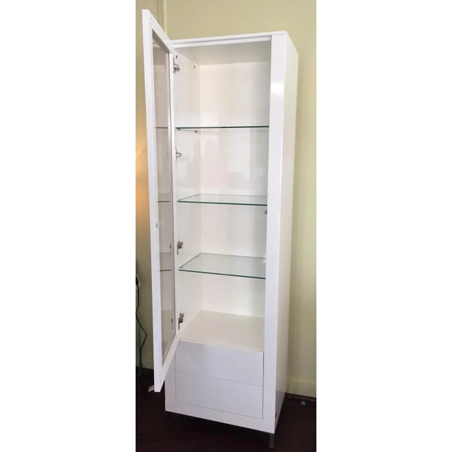 Modern white lacquer display cabinet. Touch latch door and two drawers. Chrome metal legs. Three glass adjustable shelves....