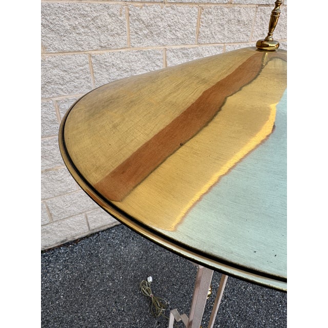 A mid-20th-century brass floor lamp. The lamp features a vertical brass stem supported by a tripod base with three splayed...