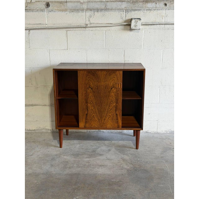 This storage piece features a clean rectilinear form and smooth sliding doors revealing interior shelves. Its minimalist...