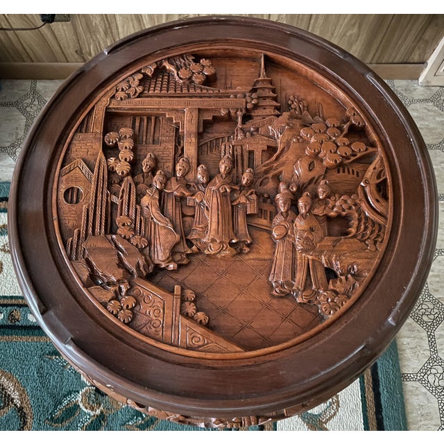 A pair of Chinese carved circular end tables depicting top courtly scenes with dragon aprons and ball and claw feet....