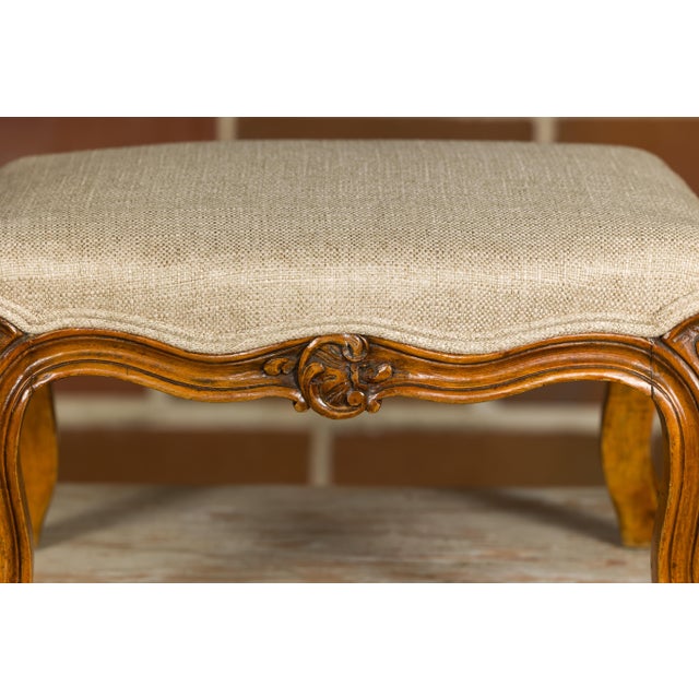 A French Louis XV style walnut footstool from the 19th century with custom linen upholstery. This exquisite 19th-century...