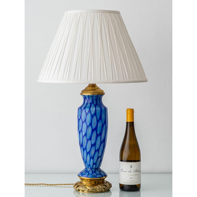A Bohemian art glass lamp: a two-tone blue blown body seated on a cast brass foot worked with leaves and tendrils, with a...