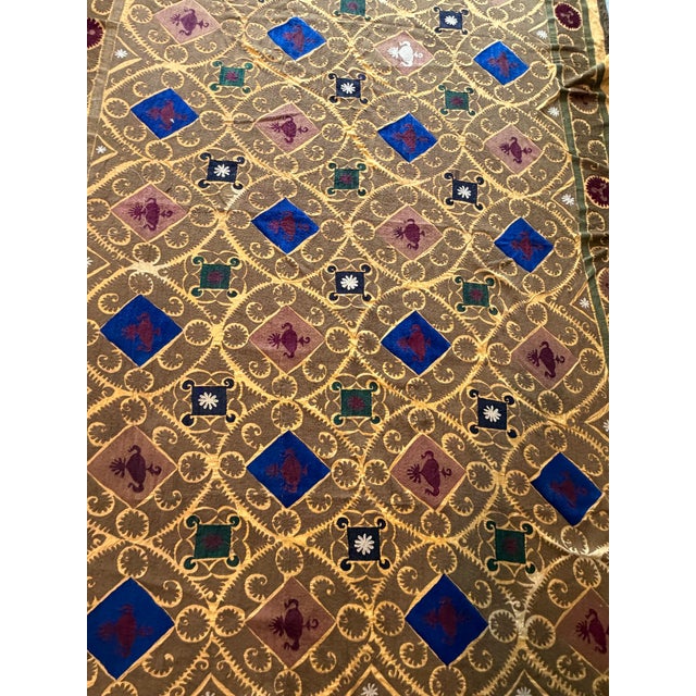 Hand-embroidered Suzani panel from Uzbekistan — a golden lattice enclosing cobalt blue diamonds, with animal and vessel...