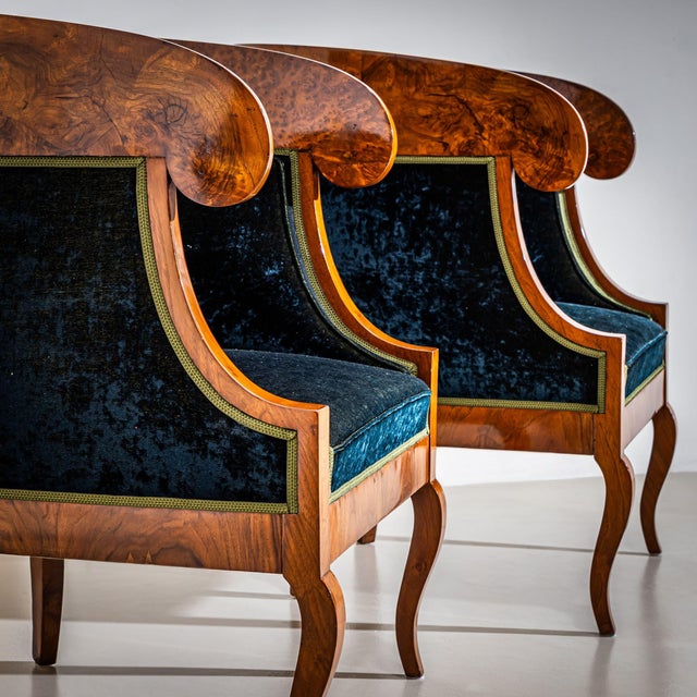 Pair of Biedermeier-style bergères with rounded backrests terminating in stylized volutes. The armchairs stand on gently...
