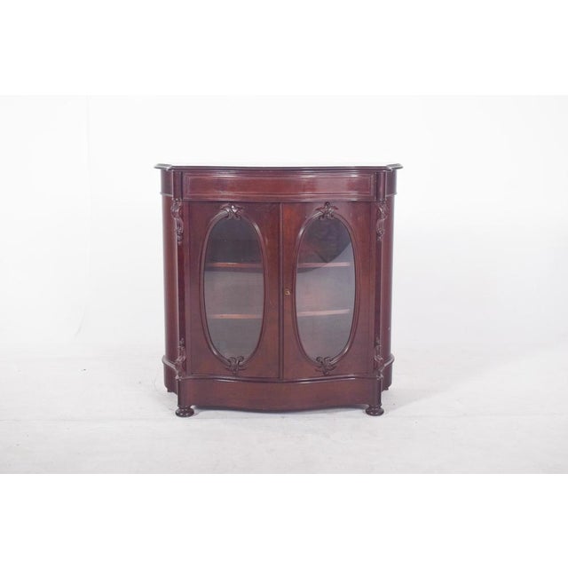 Double-door display cabinet. with a slightly curved front and two oval-glazed doors decorated with sculpted mouldings...