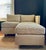 Small scale even arm occasional sofa with ottoman in textured, champagne colored upholstery on small cylindrical wooden...