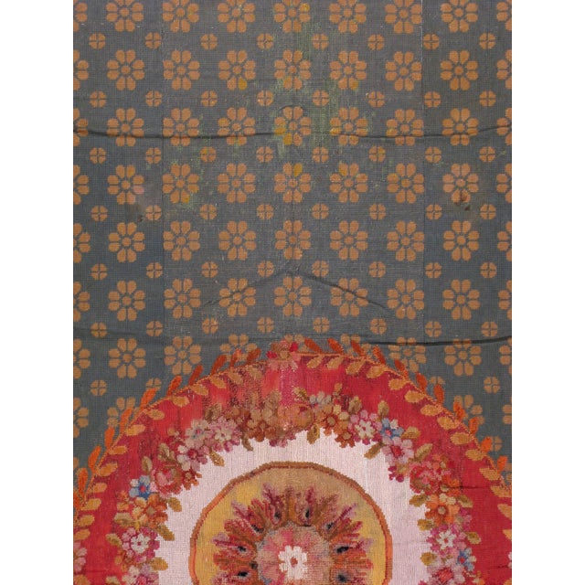 An English needlepoint carpet from the turn of the 20th century. A rosette wreath medallion serves as the focal point...