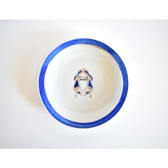 An armorial porcelain dish or shallow bowl, hand-painted with an elaborate heraldic crest featuring birds, curtains, and...