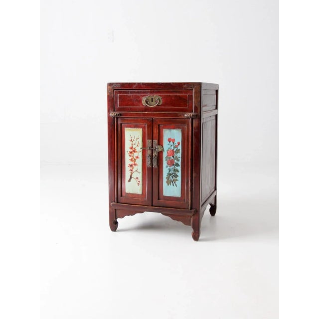 This vintage Chinese side cabinet or nightstand is crafted from lacquered wood and features delicately hand-painted...