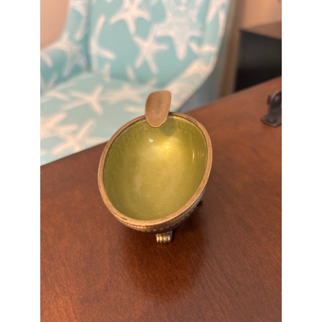A beautifully detailed vintage ashtray by Evans featuring a rich olive green marbled enamel bowl framed by ornate brass...