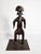 A figurative sculpture representing a stylized male figure, made of solid wood and displaying an antique dark brown to...