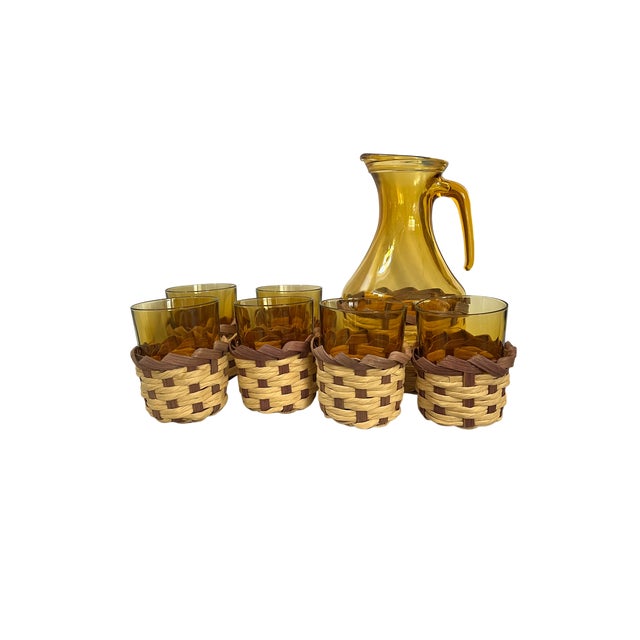 A complete seven-piece drinks set pairing warm amber glass with handwoven, two-tone wicker. The tall pitcher has a slender...
