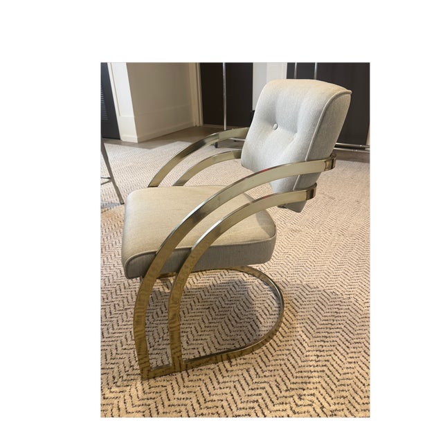 Modern and elegant dining chair with soft neutral upholstery and a gently curved, button-tufted back. The brushed gold...