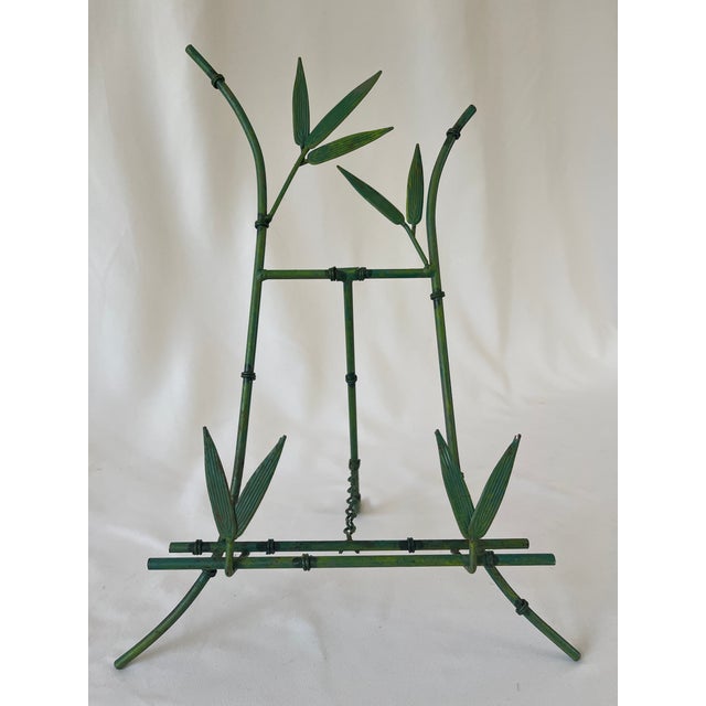 Vintage faux bamboo folding picture easel holds framed artwork. Crafted of metal and painted in a bamboo green color.