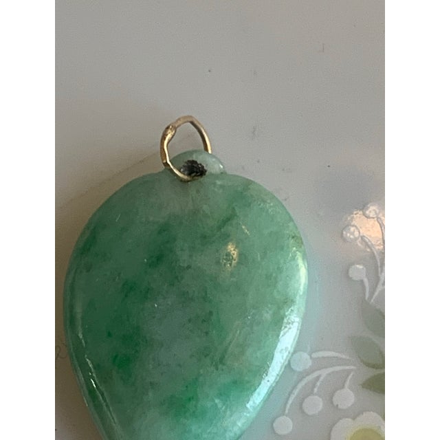 This pendant features a natural green jadeite jade carved into a heart or peach shape. In Chinese culture, this specific...