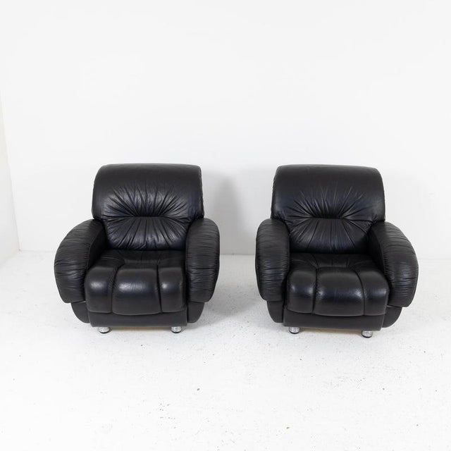 A pair of lounge armchairs with a fully upholstered frame and black leather upholstery. The seat, backrest, and armrests...