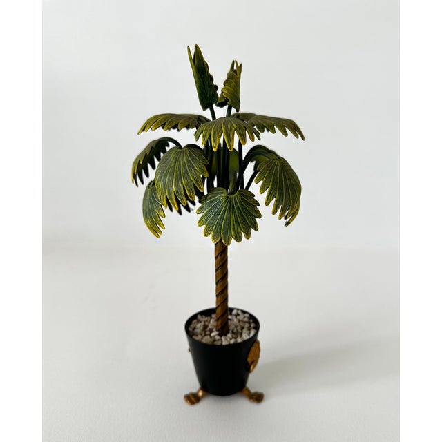 Vintage decorative tole painted metal palm tree in circular metal planter with ringed lion heads and tripod paw feet. Made...