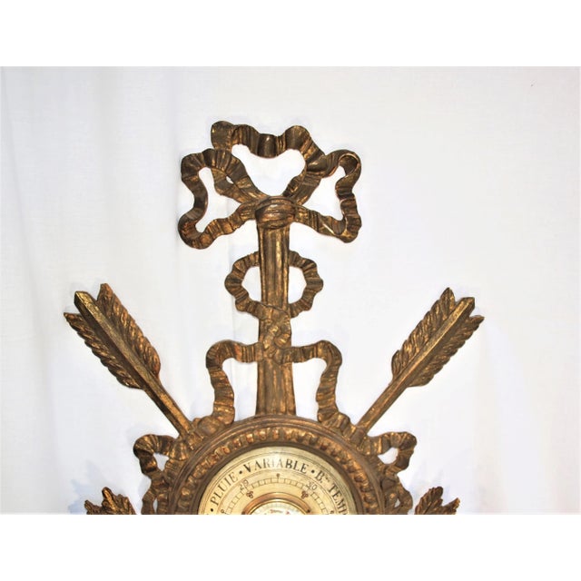 An antique French barometer set in a gold wood gilded frame. Finely carved with a bow on top, arrows on the sides and...