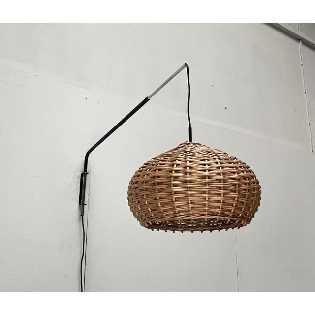 Mid-century wall lamp with a cantilevered swivel arm and rattan shade. The otherwise minimalist design of this wall lamp...