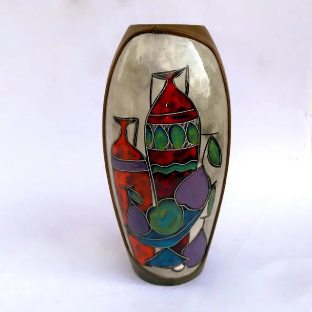 This is a ceramic vase partly covered in colored leather, featuring a still life painting. This piece has an attribution...