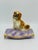 This is a vintage ceramic dog figurine featuring a small spaniel resting on a decorative tufted lavender cushion with gold...