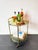A vintage bar cart in a mid-century modern style, featuring a brass frame, two removable smoked glass shelves and four...