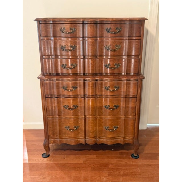 This is a tall wooden chest on chest featuring a dark amber finish, serpentine curved drawer fronts, and brass hardware....