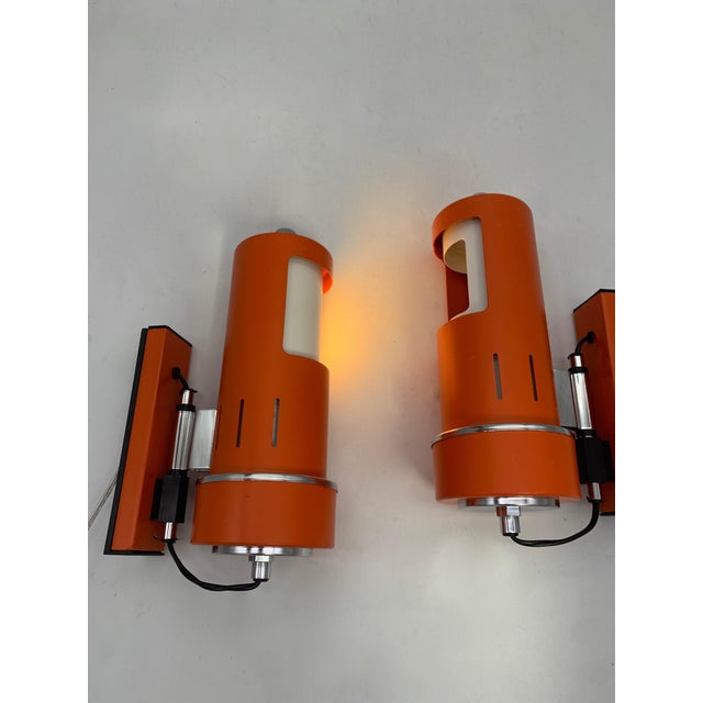 A pair of adjustable wall lamps with a distinct 1970s space-age design, featuring a cylindrical structure in orange...
