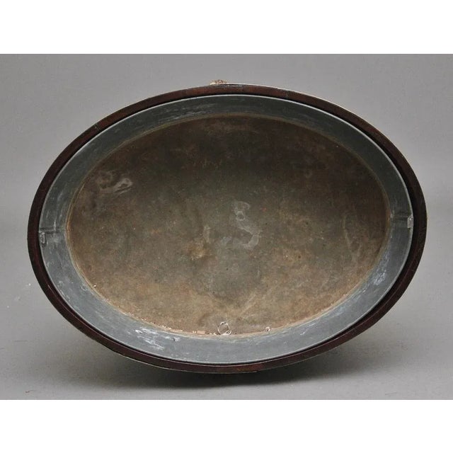 A highly decorative early 19th Century mahogany and brass bound wine cooler of an oval shape, having the original zinc...