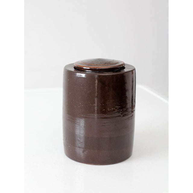 Vintage mid-century studio pottery lidded canister with a rich iron brown glaze and clean cylindrical form. The hand-...