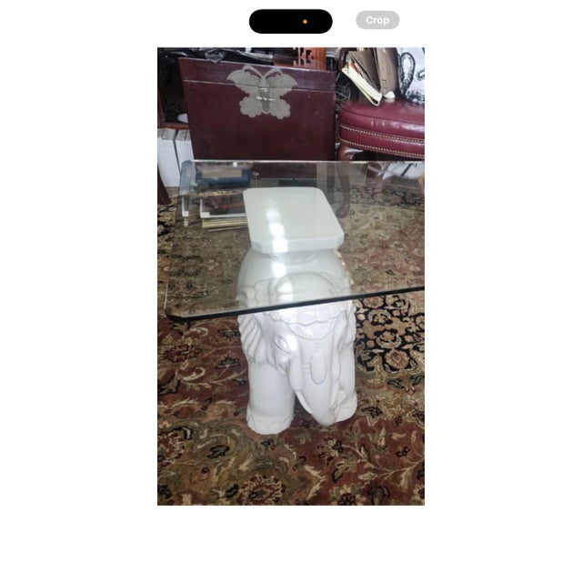 This item is a glass-top coffee table with white elephant bases, which are popular in Hollywood Regency and Chinoiserie...