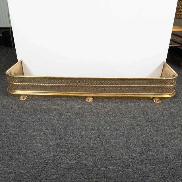 Perforated brass fireplace fender with cast animal foot and rope details.