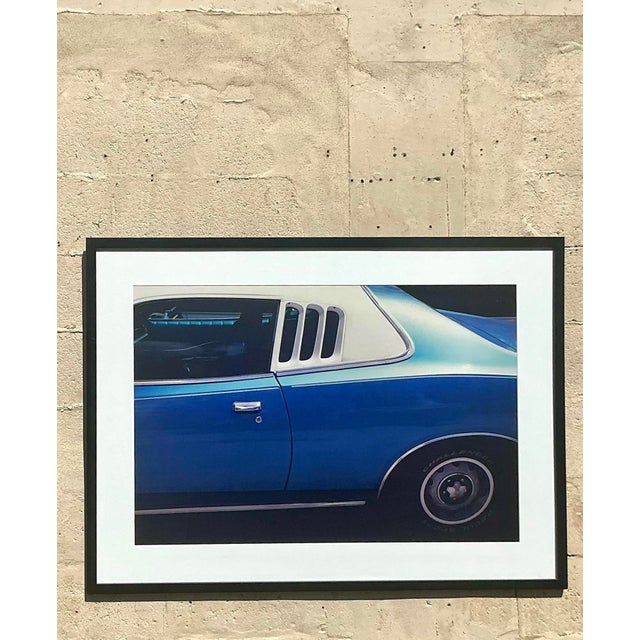 This bold photographic print captures the sleek side view of a vintage blue muscle car, highlighting its curves, chrome,...