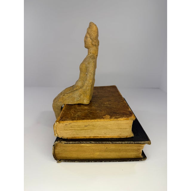 A small ancient terracotta statuette of a seated woman, possibly greek or roman. Appears to be formed from brownish red...