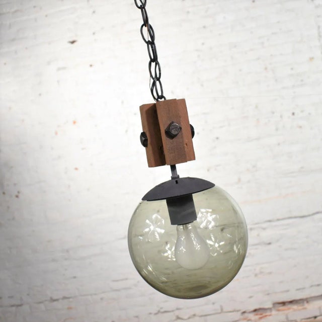 Handsome mid-century modern NOS (new old stock) slightly brutalist or rustic black, wood, and smoked glass globe pendant...
