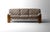 Three-seater sofa with a solid walnut frame. Four broad, rounded legs carry a curved back rail that stays visible behind...