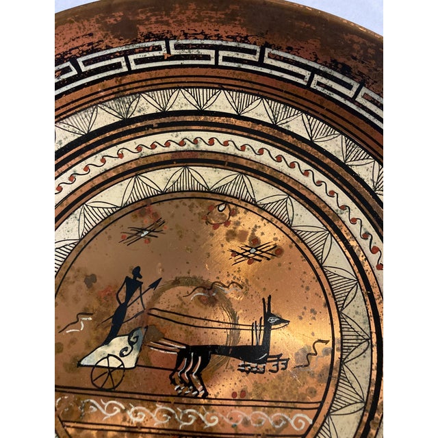This vintage round metal copper plate showcases a finely detailed classical chariot scene framed by layered geometric and...
