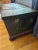 A rustic antique wooden storage chest with charming hand-painted decoration. The piece features a deep green base accented...