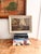 charming mid-century oil painting depicting sailboats moored in a picturesque harbor, with waterfront cottages and small...