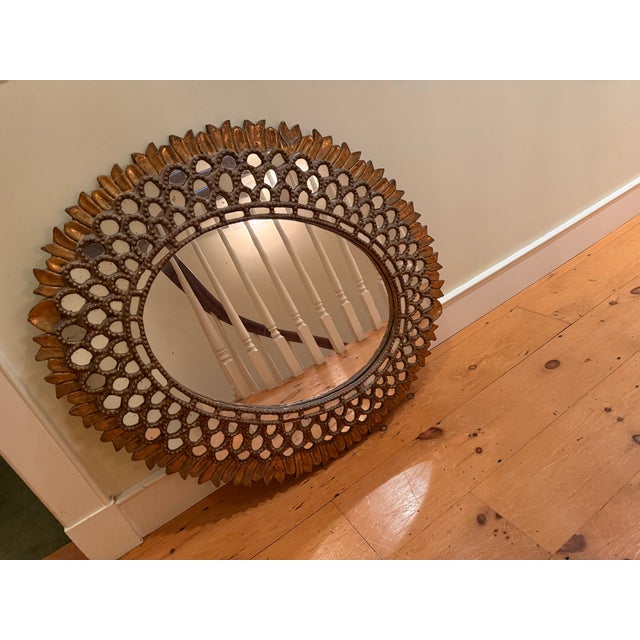 A striking vintage Spanish Colonial-style sunburst mirror from Peru. The oval mirror plate is framed by a hand-set ring of...