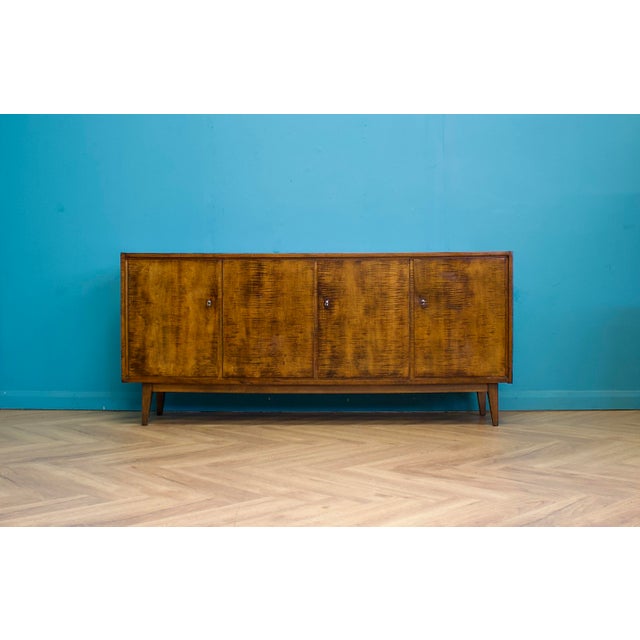 Four door sideboard in figured birch veneer with a walnut-effect finish, raised on tapered legs. Clean front with no...