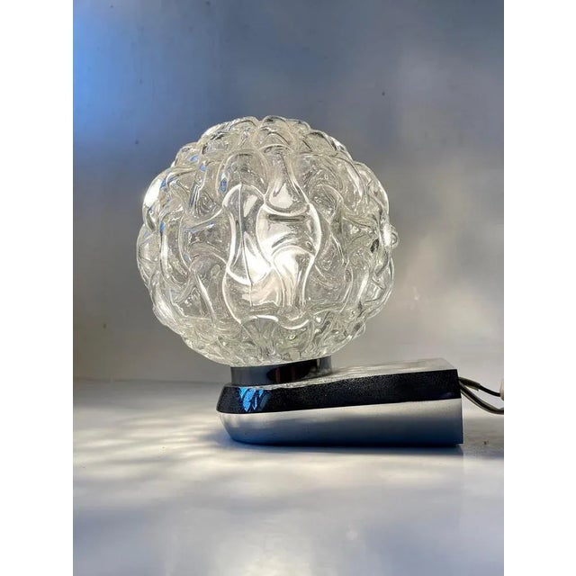 Chromed steel wall light featuring a cast clear spherical glass shade. Suitable for installation in moist environments:...