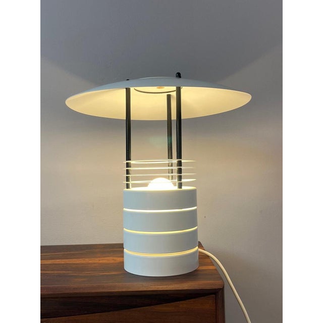 The white metal table lamp by Jørgen Buchwald for Laterna Danica impresses with its clean, timeless design. The metal is...