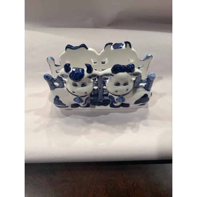 Charming hand-painted Delft Blue ceramic napkin holder featuring a cheerful cow couple dressed in classic Dutch farm...