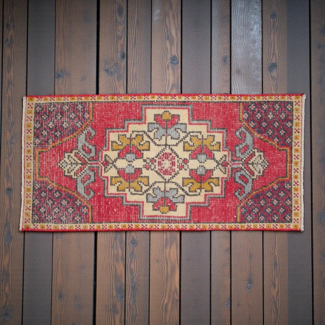 This striking vintage Anatolian mat instantly captivates with its bold, geometric tribal patterns and vibrant crimson...