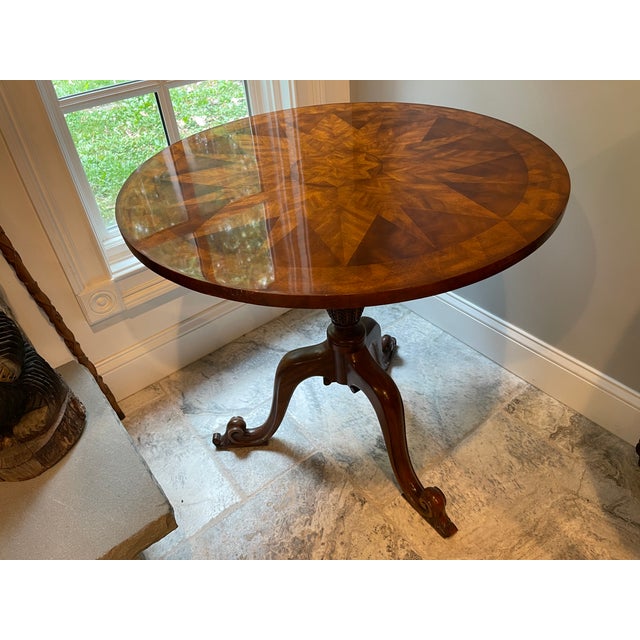 A vintage round accent table with an inlaid starburst marquetry top and carved pedestal tripodal base. Product...