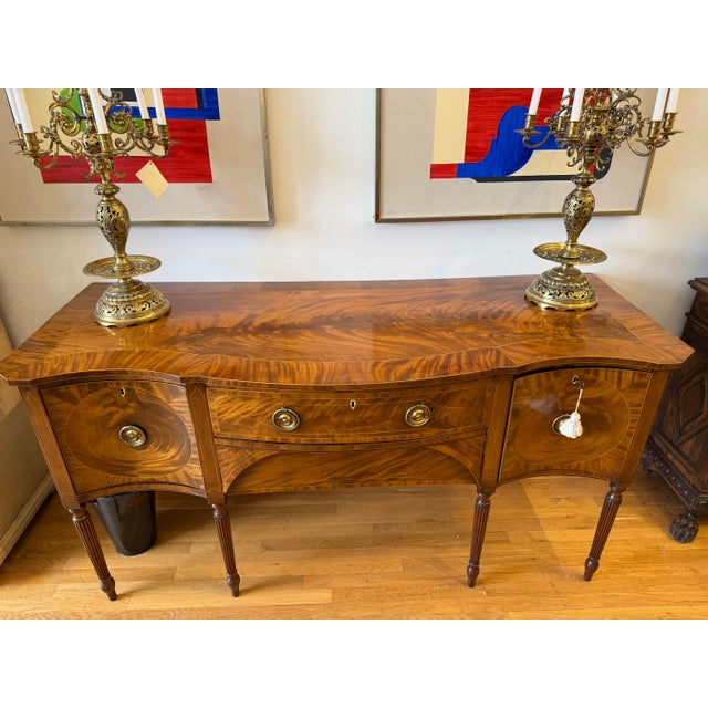 A rare and resplendent example of late 18th-century British craftsmanship, this early Sheraton period serpentine sideboard...